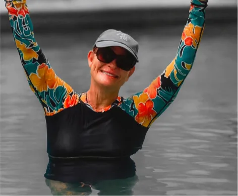 Kim Bushell in the pool holding a yellow pool noodle overhead