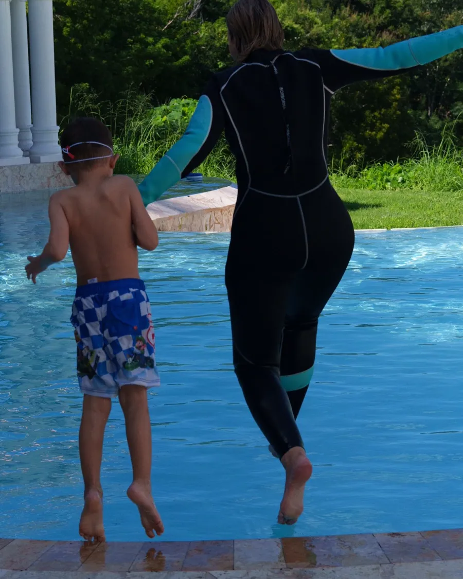 Swim instructor and a young swimmer jumping into the pool together, hand in hand